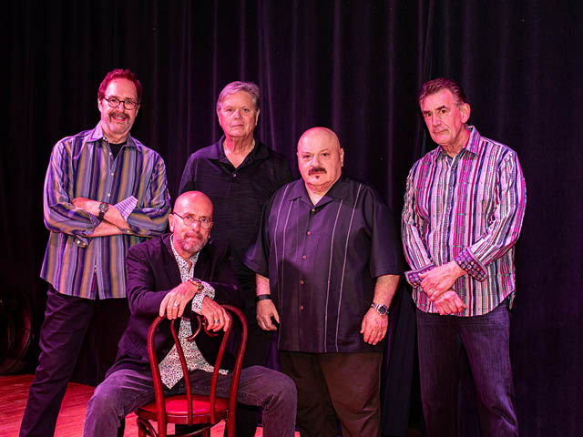 Five white men on a stage posing for the camera
