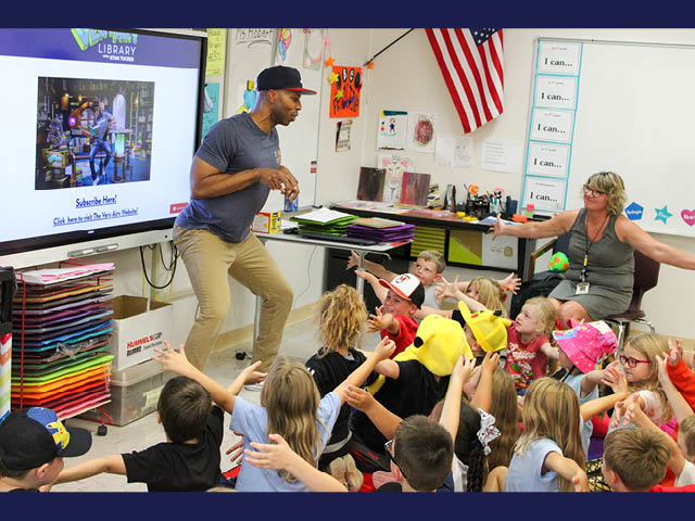 Author Stan Tucker stands in front of a classroom and appears to be hopping like a bunny while students hold their arms up high