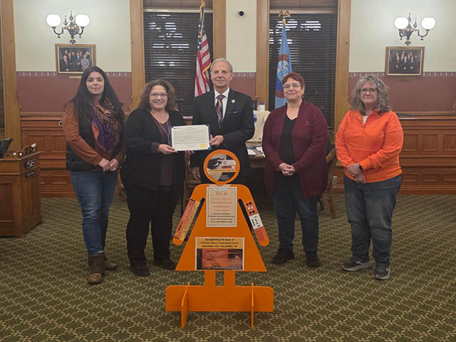 Four women stand with Mayor Corradino with the Orange Lady display and the mayoral proclamation