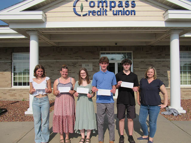5 scholarship award winners standing with checks in front of the Compass FCU building. A bank employee stands to the far right.