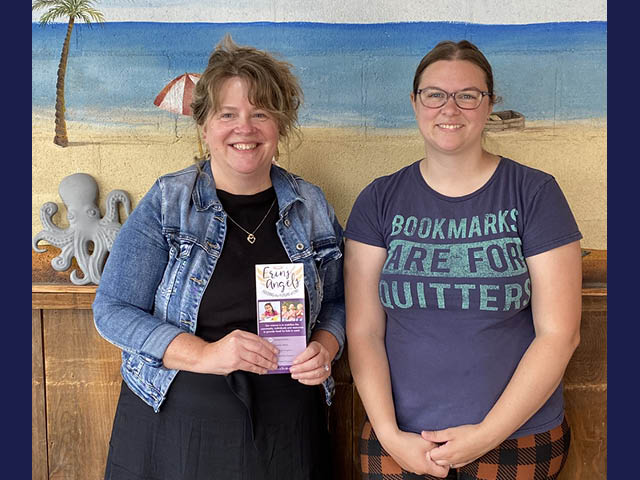 Two white women standing in front of a beach mural