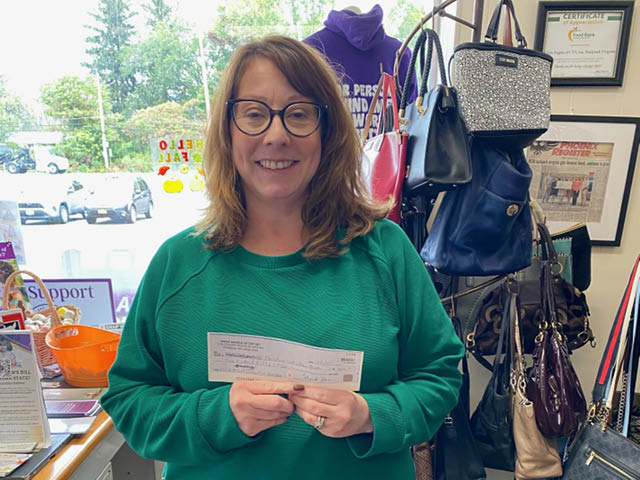 A white woman in a green sweater holding up a check