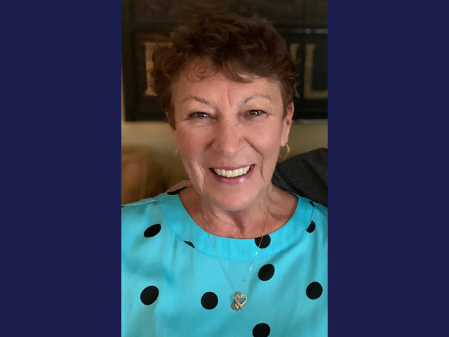 A smiling white woman wearing a blue shirt with black polka dots