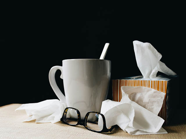 A coffee mug, tissue box, crumpled tissues and glasses set on a table