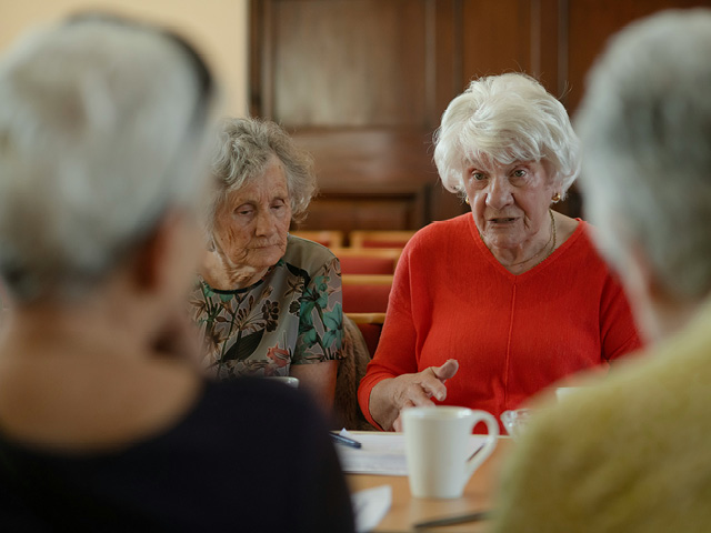 Senior women sitting at a table in a church-like atmosphere with a cup of coffee in front of them