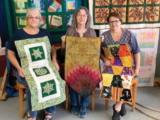 three women standing with their quilts
