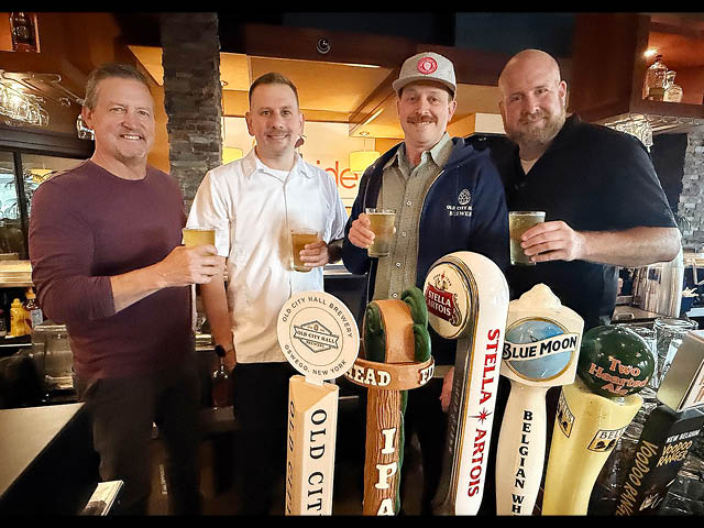 Four men standing at Dockside's bar with glasses of Lighthouse Lager and smiling