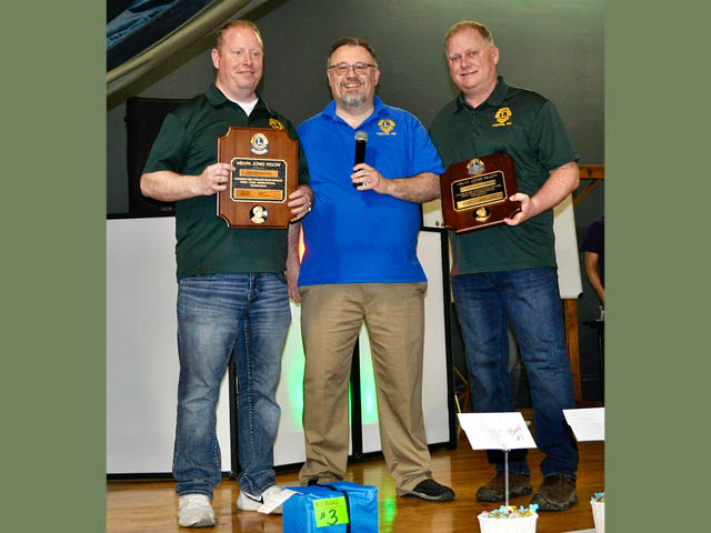 Three men standing on a stage, two holding awards