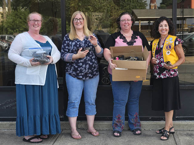 Four white women standing on a sidewalk with a box of glasses