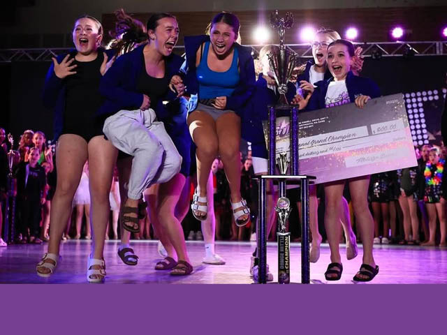 Dancers jumping up and down on stage with their award and giant presentation check