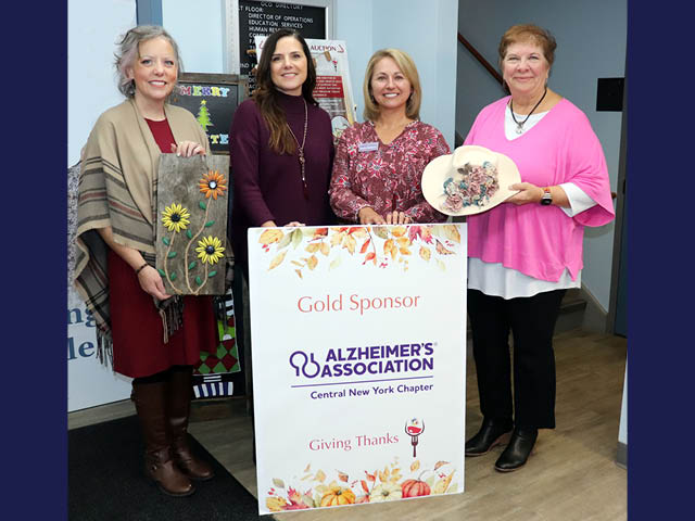 Four white women standing in front of a sign that recognizes the Alzheimer's Association as a gold sponsor of Giving Thanks