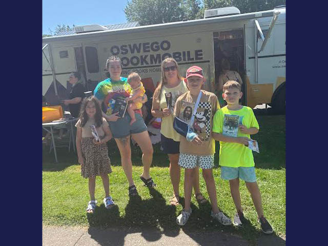 Kids and adults standing in front of the Oswego Bookmobile with books in their hands