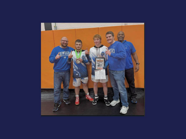 Several wrestlers and coaches holding up a medal and a plaque