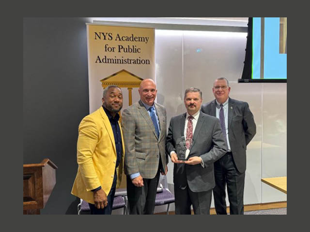 Four men standing in front of NYS Academy for Public Administration banner