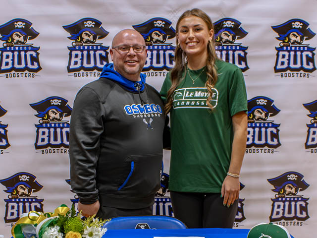 Ted Beers stands next to senior Peyton Bond in front of a Buc Booster backdrop