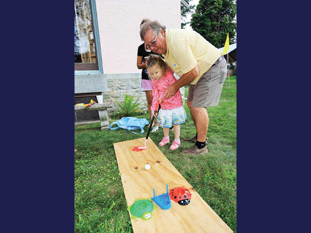 A toddler hitting a ball on the lawn at RBH house, being guided by an older man