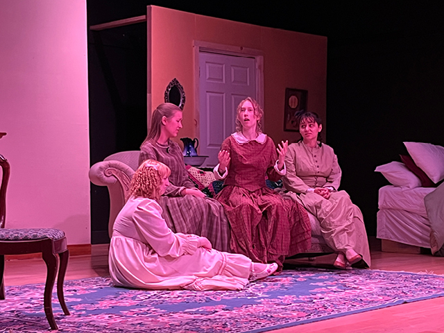 Four women in 1860s period dress talking on a couch