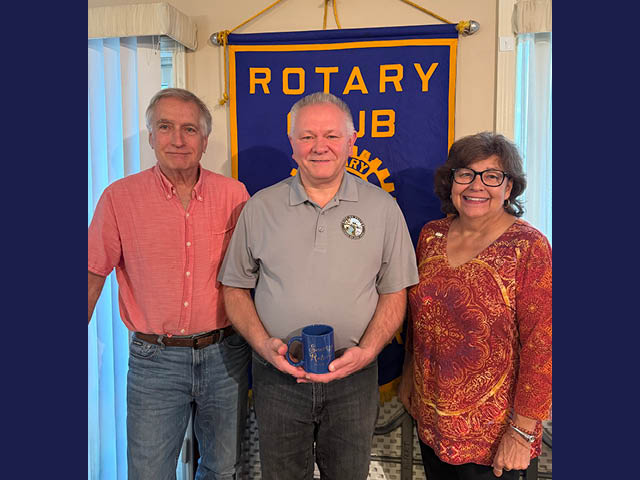Three people standing in front of a Rotary banner