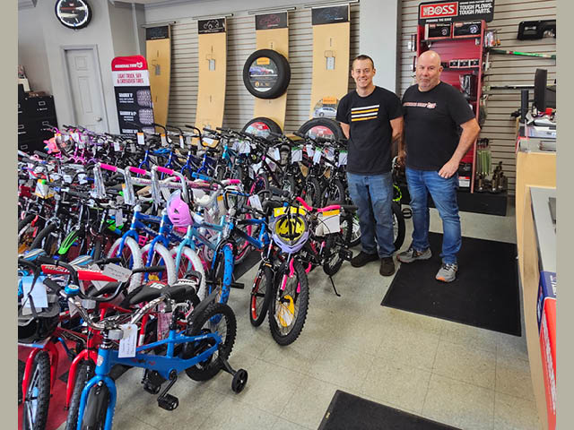 Two men stand next to dozens of children's bikes