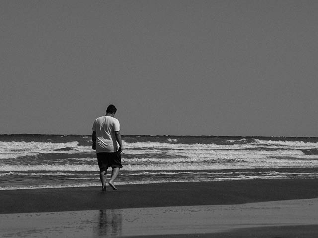 A grayscale image of a man walking towards water on the beach