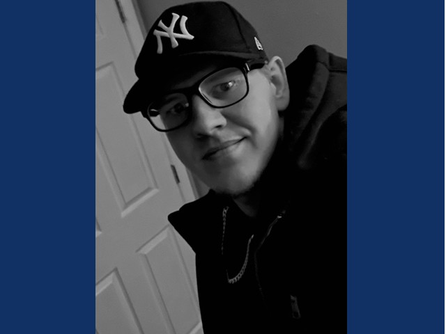 Young man smiling with glasses, NY baseball cap and dark hoodie.