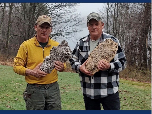 tow men holding large rock feet in a field
