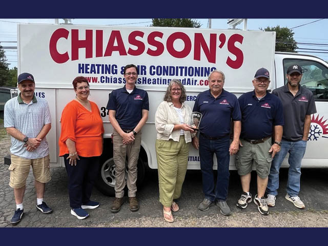 Photo of a group of people standing in front of a Chiasson's van; Tammy Thompson is in the center holding a plaque