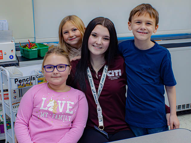 A high school student in a CiTi polo shirt poses with three elementary-aged students