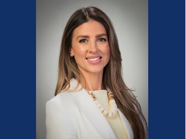 Young woman with long brown hair smiling in a white suit  with beaded necklace
