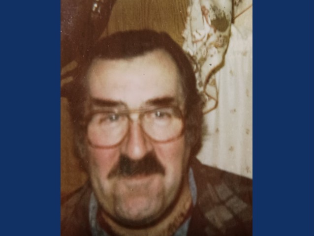 Older photo of man with dark short hair and dark thick mustache with round glasses and flannel shirt.