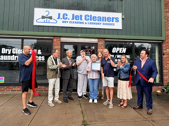 People holding a cut ribbon in front of the JC Jet Cleaners storefront