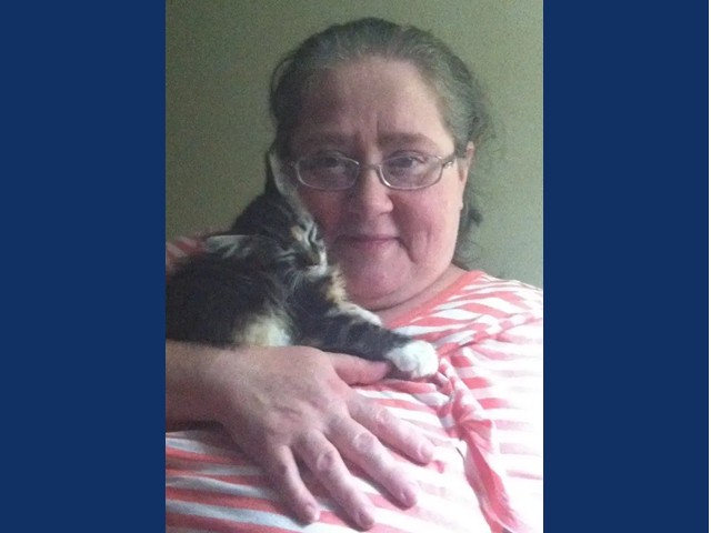 Woman with dark graying hair pulled back with glasses and pink and white striped shirt holding a small dark tiger kitten