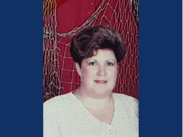 Woman with short dark hair wearing white top in front of deep red wall with fishing net decor hanging on it