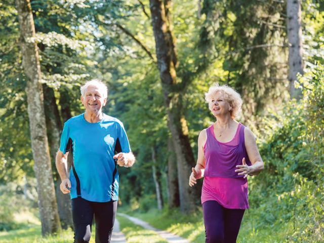 An older man and woman running on a trail through the woods