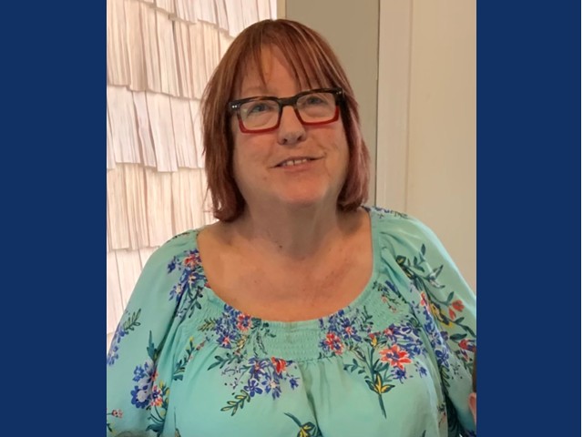 woman with brownish red shoulder length hair wearing glassed in a light blue floral shirt