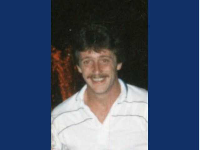 Young man with dark wavy hair and mustache smiling in white polo with stripes