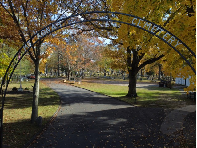 Trees in fall at gate of cemetery with the wrought iron arch over the roadway