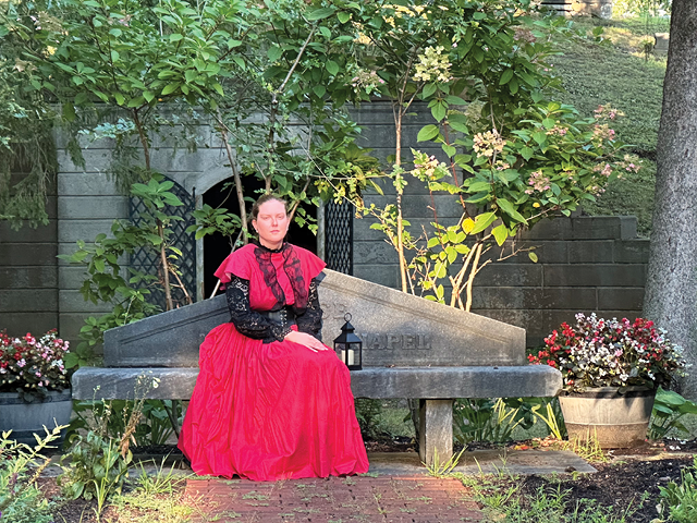 A woman in period red dress sits on a bench in Mt. Adnah Cemetery