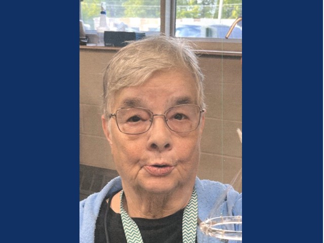 woman with round glasses and short gray hair in black t-shirt with cardigan over top and lanyard around neck