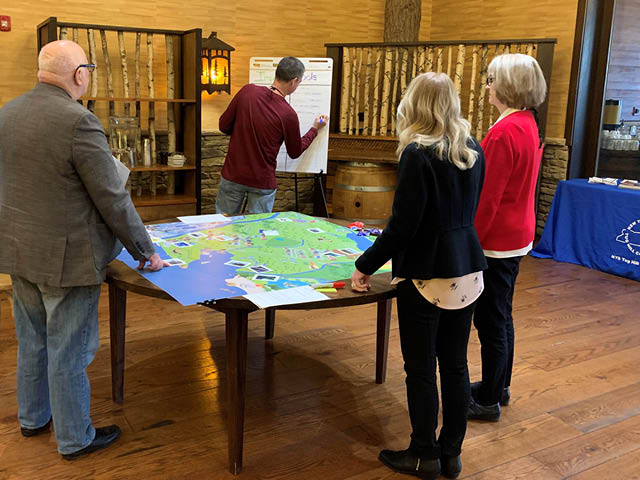 Photo of people standing at a table with a map and facing an easel with paper