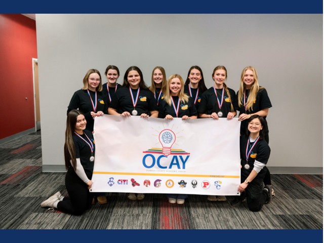 Ten teens standing around an OCAY banner, medals around their necks in all black.