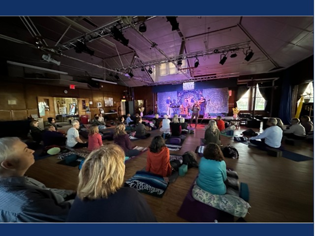People sitting on floor mats and blankets listening to performance on stage