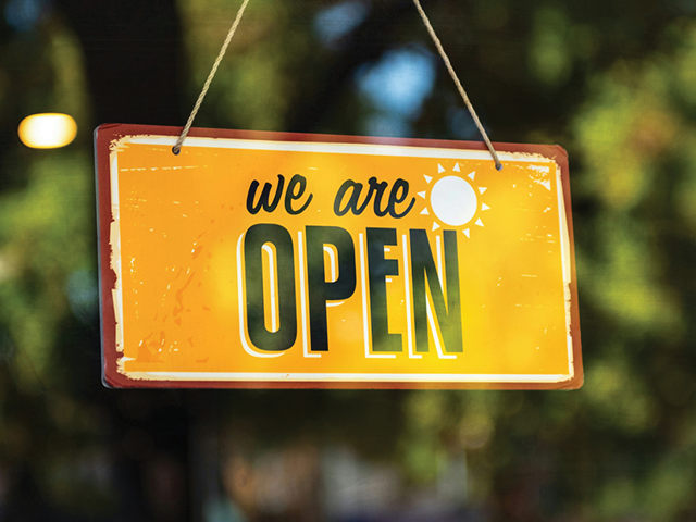 Photo of a yellow sign that says "We are open" in a window reflecting greenery