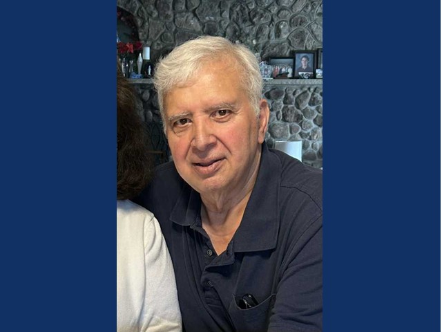 Gentleman with gray hair parted on side with black collared button up shirt.