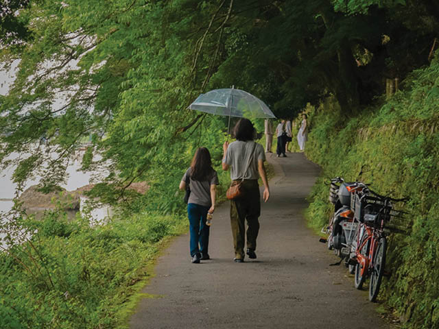 People walking on a paved trail next to a body of water; bikes are parked next to the trail