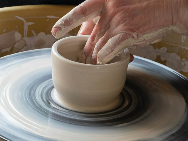 Person shaping a cup on a pottery wheel