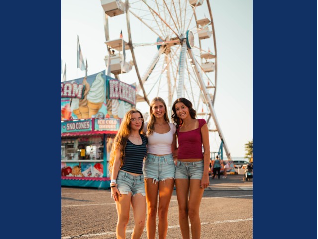 Three teen girls in front of ferris wheel.