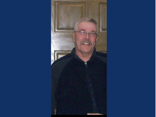 Man with short silver hair, glasses and mustache wearing a dark zip up