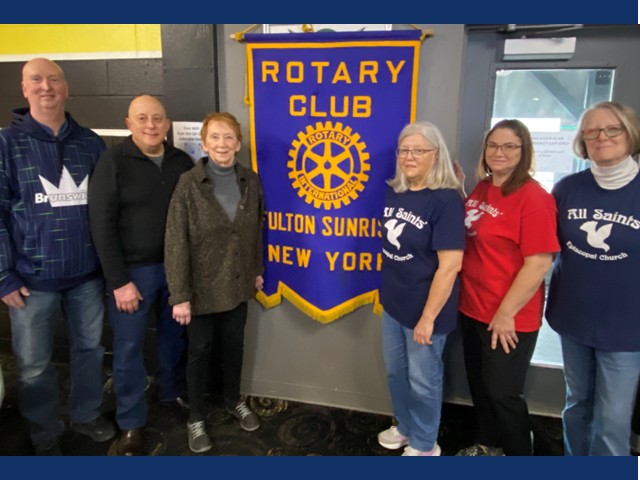 Six men and women standing in front of Rotary Club sign.