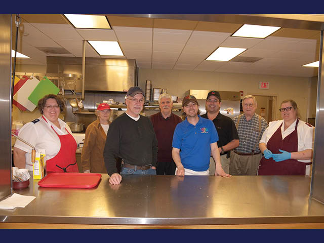 A group of people from the Salvation Army and Rudy's Drive-In standing in a kitchen at the Salvation Army